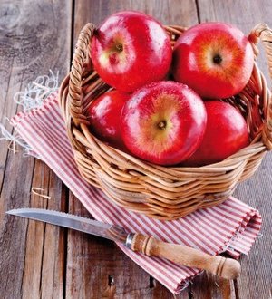 Red organic apples in a straw basket on wooden background Healthy organic red apples in a straw basket and knife on a wooden background