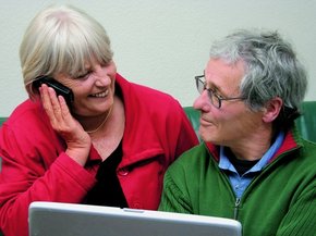 [Translate to South Africa English:] Elderly couple on front f a laptop looking at each other while she is talking on the phone